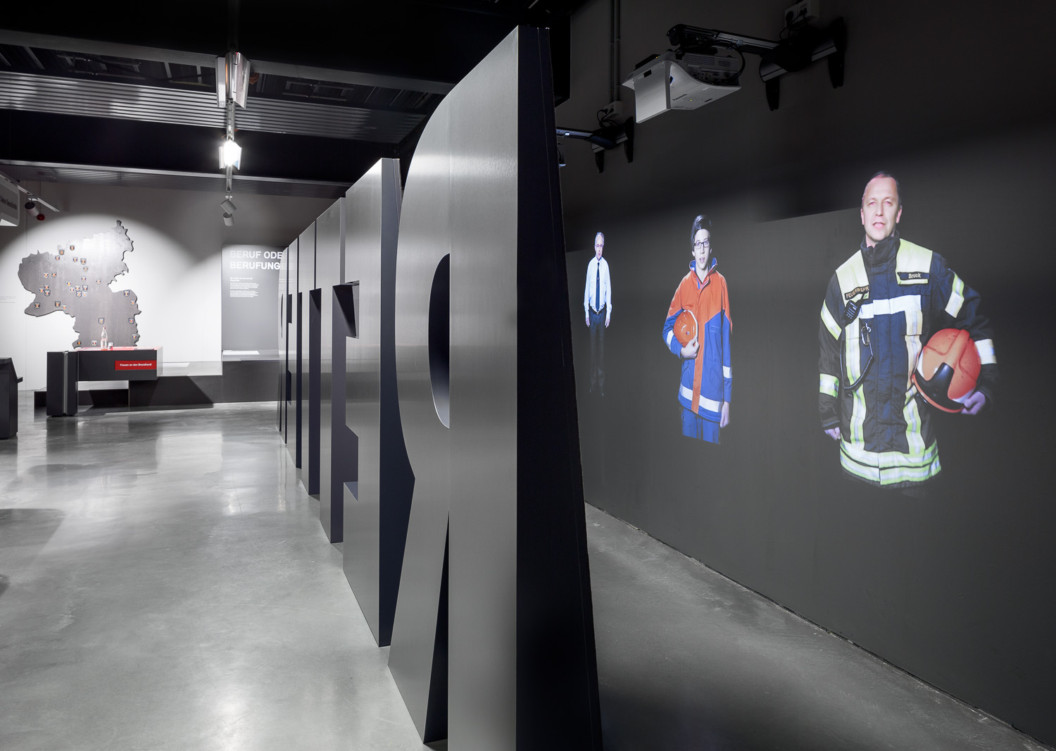 Large black letters form the word "rescuers" and serve as room divider. Behind them are projections of various firefighters.