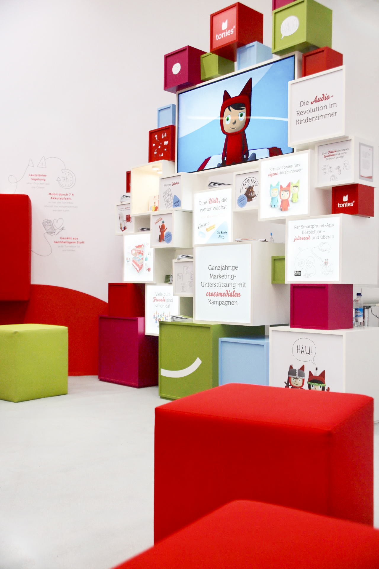 Colourful cube in front of wall with screen showing Tonie mascot